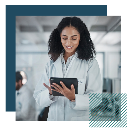 A woman wearing a lab coat is looking down at a tablet computer and smiling